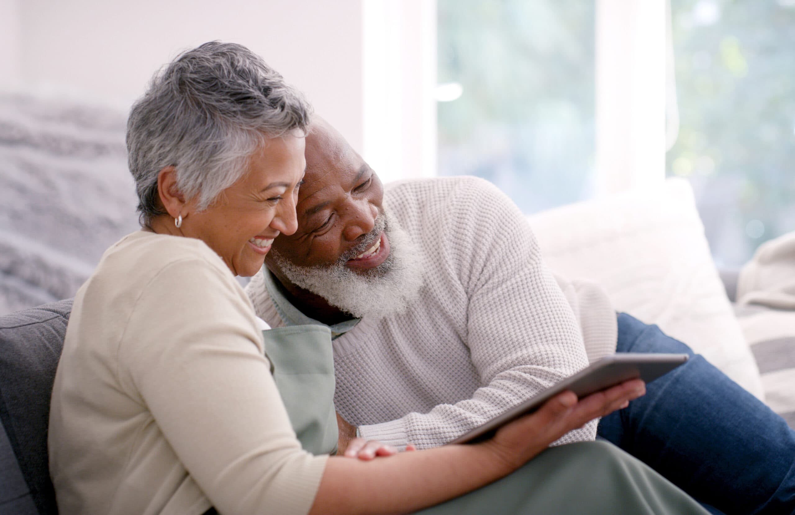 A happy couple browsing the internet on a tablet, cozy on the couch.